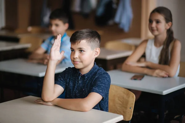 İlkokuldaki mutlu küçük çocuklar. Erkekler ve kızlar okuyor. Çocuklar el kaldırır — Stok fotoğraf