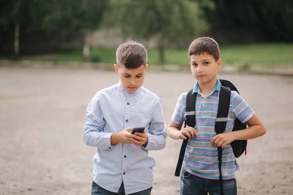 Dos chicos juega juegos en línea después de las clases escolares. Los jóvenes sonríen y usan el teléfono — Foto de Stock