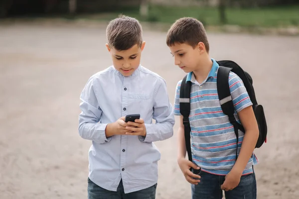 Due ragazzi gioca giochi online dopo le lezioni di scuola. Giovani ragazzi sorridono e usano il telefono — Foto Stock