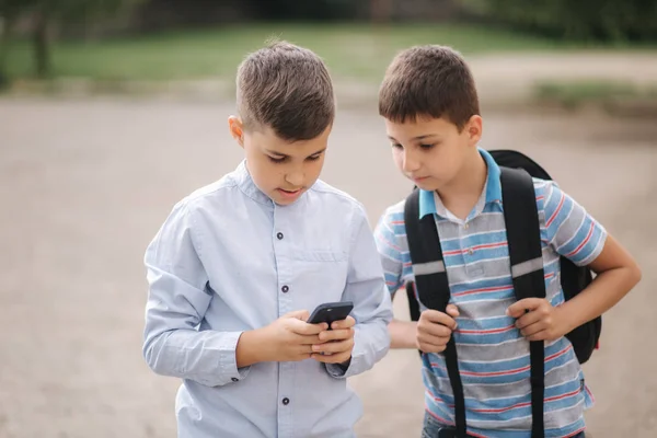 Двоє хлопчиків грають в онлайн ігри після уроків. Молоді хлопці посміхаються і користуються телефоном — стокове фото