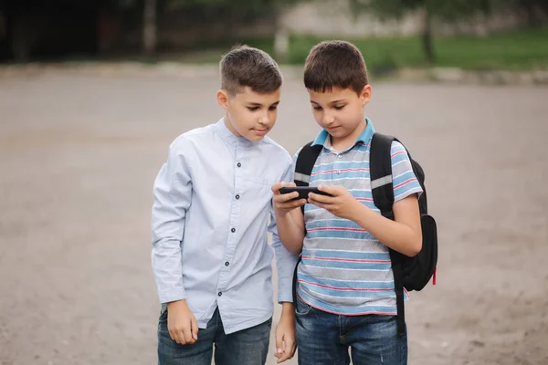 Två pojkar spelar online-spel efter skolklasser. Unga pojkar leende och använda telefonen — Stockfoto