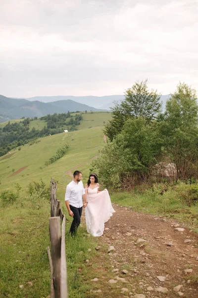 緑の斜面、丘の上に立っている美しい若い結婚式のカップル。カルパチア山脈の新郎と花嫁 — ストック写真