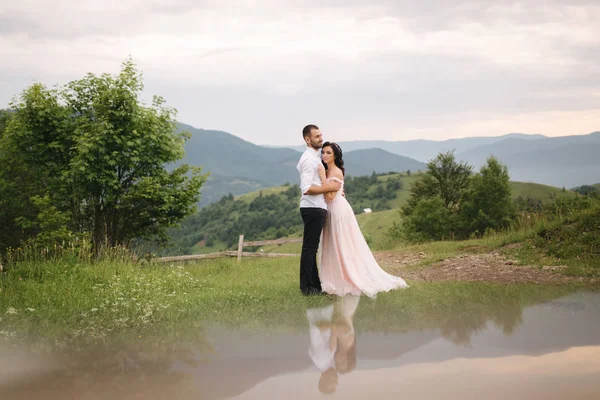 Casal jovem bonito de pé na encosta verde, colina. Noiva e noivo nas montanhas dos Cárpatos. Homem beijo mulher na testa — Fotografia de Stock