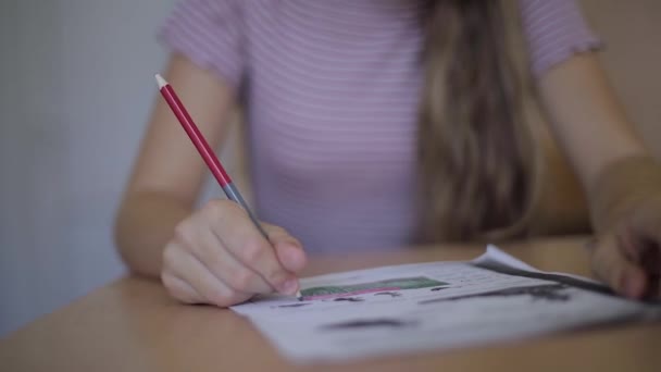 Happy schoolgirl sitting at desk and writing in exercise book — Stock Video