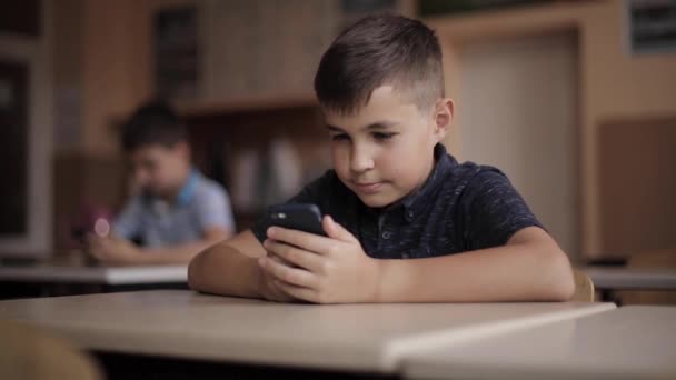 Милый мальчик пользуется телефоном во время урока. Два студента в классе — стоковое видео