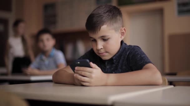 Lindo niño usa el teléfono durante la lección. Dos estudiantes en clase — Vídeos de Stock