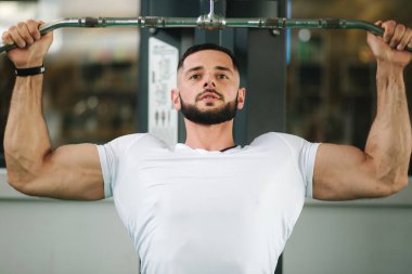 Genç bir atlet spor salonunda eğitiyor. Sırt ve göğüs kaslarının gösterir