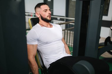Adam spor salonunda bacak yetiştirir. Yakışıklı sakallı vücut geliştirmeci eğitimi