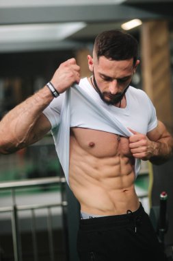 Genç atlet spor salonunda fotoğraf için bir gövde ile poz. Vücut geliştirmeci, pompalı kasları ile atlet, meme ve kol kurtarma. Adam göstermek karın kasları