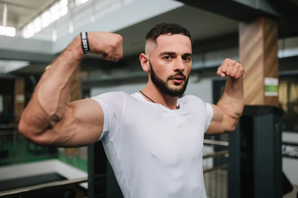 Jovem atleta posando com um tronco para fotografia em um fundo de ginásio. Fisiculturista, atleta com músculos bombeados — Fotografia de Stock