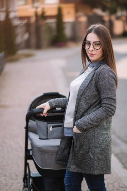 Küçük bebeği ile yürüyen çekici genç anne. Anne ile yenidoğan bebek içinde Pram