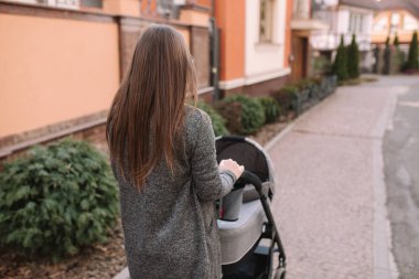 Küçük bebeği ile yürüyen çekici genç anne. Anne ile yenidoğan bebek içinde Pram