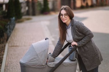 Genç Anne yürümek ile kız içinde Stroller. Annem bebeği önemsiyor. Anne Puset için bakmak ve bebek uyku yardım