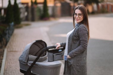 Aile, çocuk ve ebeveyn konsepti-parkta puset ile mutlu anne. Güneş gözlüğü ve şık gri ceket ile anne