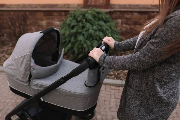 Madre joven caminando con su bebé recién nacido en cochecito. Un cochecito gris. Hermosa mamá en gafas de sol — Foto de Stock