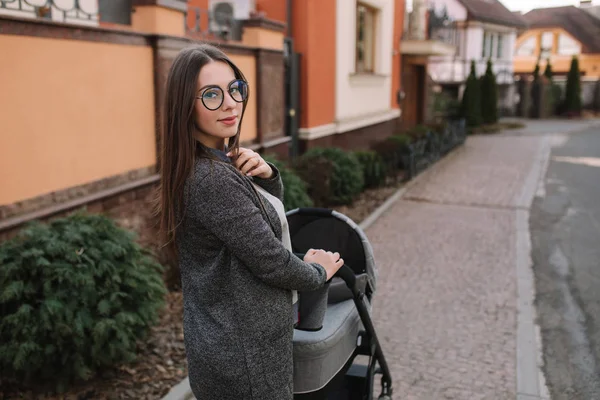 Attractive young mother walking with her little baby. Mom with newborn baby in pram — Stock Photo, Image