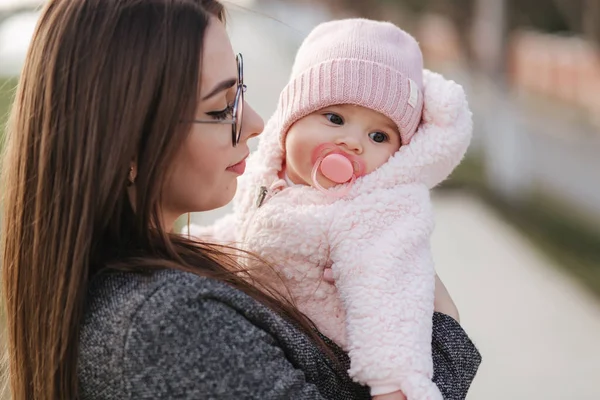 Portret van moeder en haar kleine baby meisje. Mooie moeder en schattige baby. Moeder HUD haar dochter. Baby gekleed in peanch kleur hoed en tepel speelgoed — Stockfoto