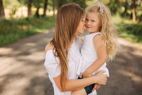 Aantrekkelijke moeder en blond haar dochter zit op weg in de buurt van grote steegje. Ze glimlachen en kijken naar natune. Vooraanzicht — Stockfoto