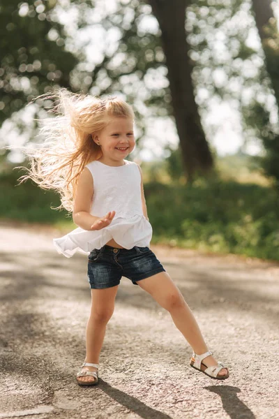 금발 머리 춤과 따뜻한 여름 날에 골목을 통해 점프와 쾌활 한 귀여운 소녀 — 스톡 사진