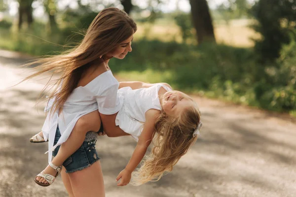 Маленька дівчинка грає з мамою в парку в літній день під час заходу сонця крутиться навколо — стокове фото