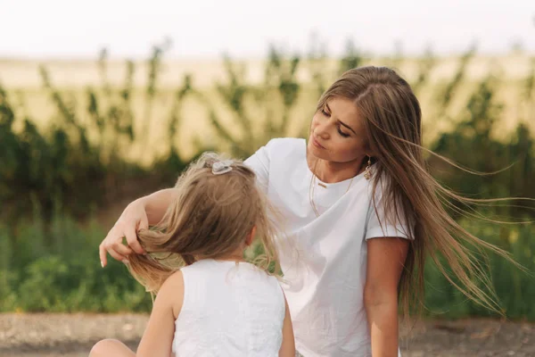 Attractive Mom and blonde hair daughter sits on road near big alley. They smile and look to natune — Stock Photo, Image