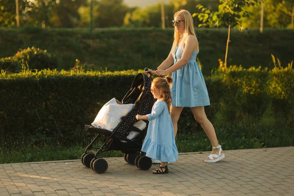 Little daughter helps mom push the baby carriage. Happy family — Stock Photo, Image