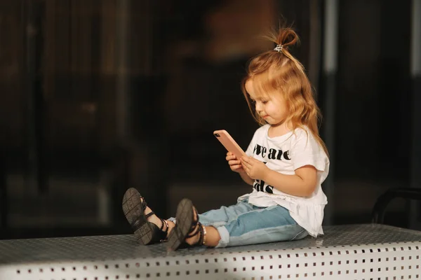 小女孩坐在长椅上,在商场附近用手机 — 图库照片