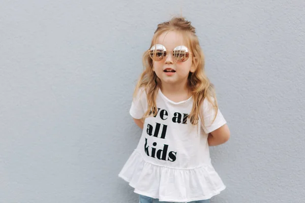 Kleines Mädchen mit Sonnenbrille posiert für Fotografen. Blonde Haare weiblich Kind unsittlich — Stockfoto