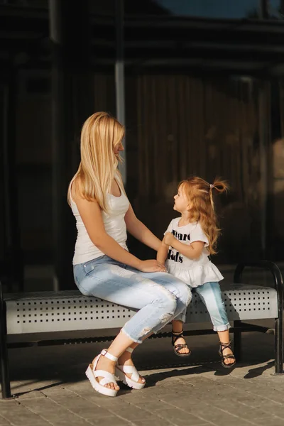 Mother and daughter outdoors in city. playing and having fun. Fashion happy mother and child daughter having fun together in the city. They are sitting on the bench near the mall — Stock Photo, Image