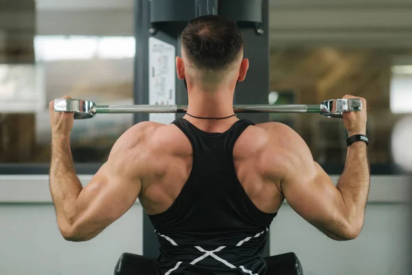Молодой спортсмен тренируется в спортзале. Показывает мышцы спины и груди. Вид сзади — стоковое фото