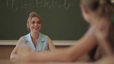 Çocukların önünde kadın öğretmen. Sınıfta ki güzel öğretmen masada oturup çocuklara soruyor. eğitim, ilkokul, öğrenme ve insan kavramı