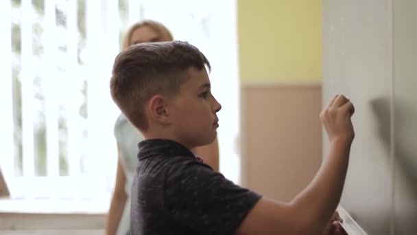 귀여운 소년은 칠판의 교실 배경에 서있다. 교육. 초등학교 — 비디오
