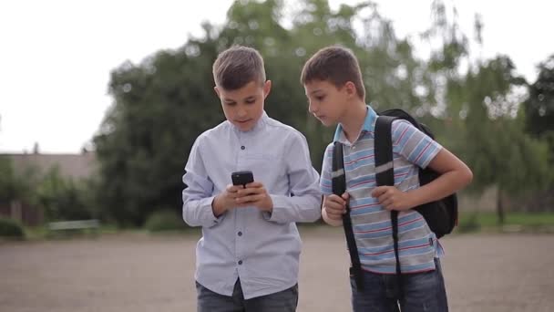Δύο αγόρια παίζουν διαδικτυακά παιχνίδια μετά τα σχολικά μαθήματα. Νεαρά αγόρια χαμογελούν και χρησιμοποιούν το τηλέφωνο — Αρχείο Βίντεο