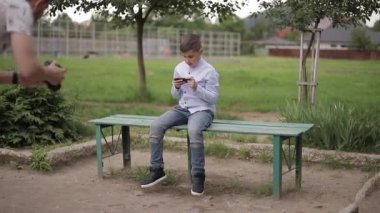 Handome genç çocuk Bench üzerinde oturan ve okul molası sırasında online oyunlar oynamak