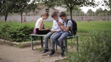 İki erkek ve bir kız okul tatilinde telefonlarını kullanıyor. Tatlı çocuklar bankta oturup online oyunlar oynuyorlar.