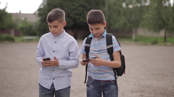 Dva kluci hrají on-line hry po školních hodinách. Mladí hoši se usmívají a používají telefon — Stock video