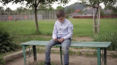 Handome genç çocuk Bench üzerinde oturan ve okul molası sırasında online oyunlar oynamak