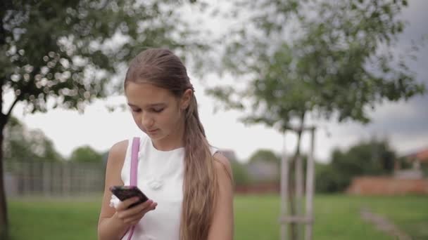 Mladá dívka používá telefon během školních prázdnin. Dívka hrát online hry — Stock video