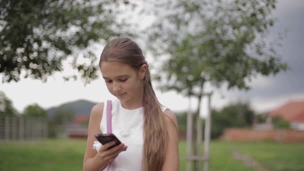 Mladá dívka používá telefon během školních prázdnin. Dívka hrát online hry — Stock video