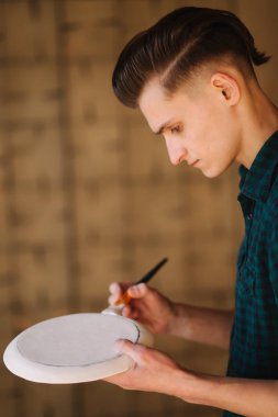 Potter seramik tabakta süs yapıyor. Profesyonel erkek çömlekçi seramik ürün üzerine bir kalem çizer