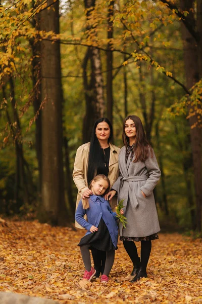 Mom and two daughter have fun in ther park. Youngest daughter collect leaves and smile. Happy family walking in the forest