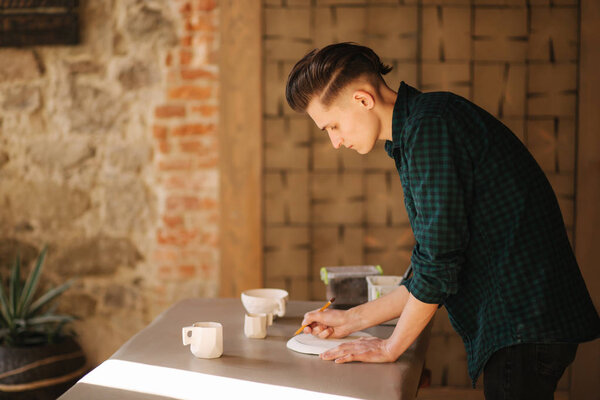 Potter making ornament on ceramic plate. Professional male potter draw a pencil on ceramic product