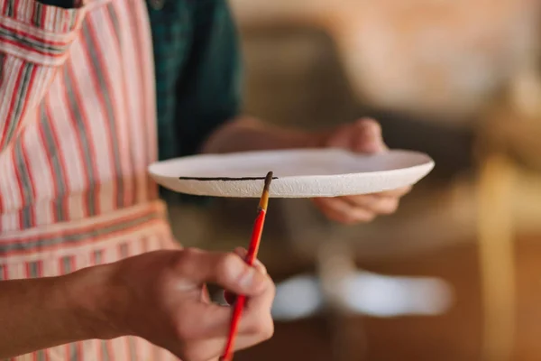 El acercamiento de los alfareros por las manos que adornan el producto cerámico. Placa en manos masculinas. Joven artista — Foto de Stock