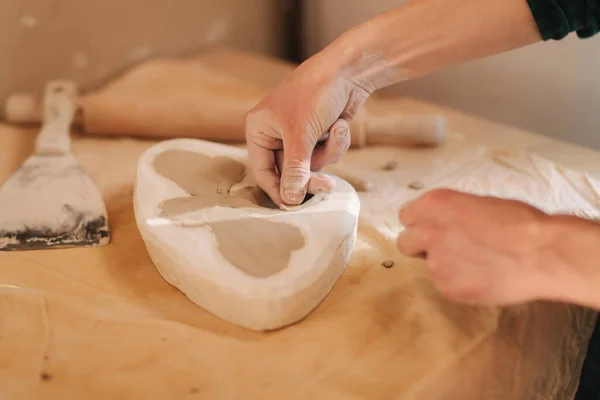 Handen van pottenbakker vul het formulier met een keramiek in de vorm van een vlinder. Sluiten van de handen — Stockfoto