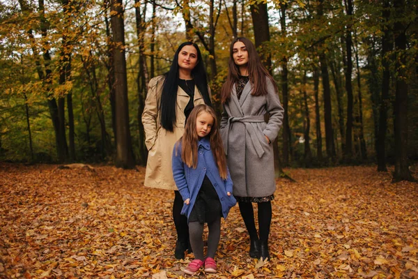 Mom and two daughter have fun in ther park. Youngest daughter collect leaves and smile. Happy family walking in the forest