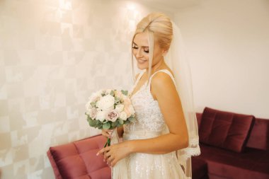 Güzel düğün elbisesi ile buket evde içinde zarif gelin. Sarı saçlı kadın güzel makyaj ve saç modeli ile