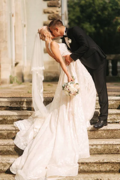 O noivo e a noiva estão nas escadas. Modelo de moda em roupas elegantes. Vestido longo branco e terno elegante — Fotografia de Stock