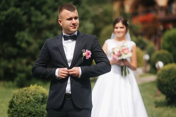 Gorgeous bröllopspar går på bak gården av par hus. Grön bakgrund — Stockfoto