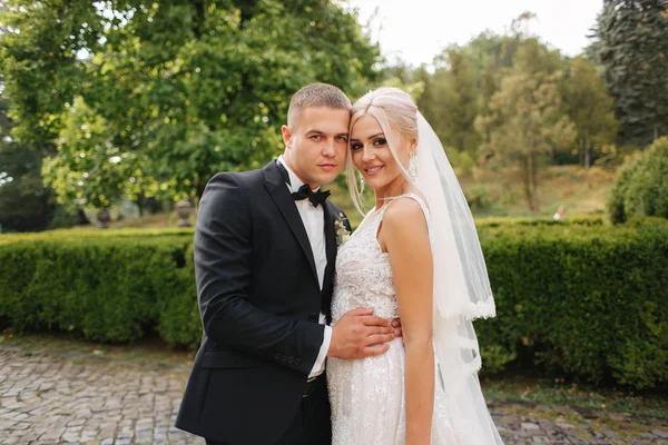 Belo casal de casamentos andando no parque. Noiva com vestido branco longo e noivo elegante — Fotografia de Stock