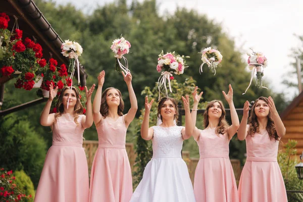 Novia feliz con ramos de dama de honor y divertirse al aire libre. Hermosa dama de honor en los mismos vestidos de pie junto a la encantadora novia en vestido de novia largo —  Fotos de Stock